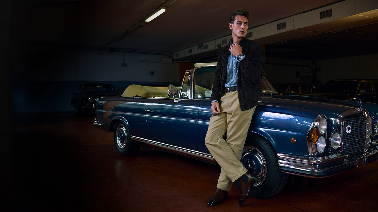 Model leaning on a classic blue convertible wearing a Q Timex® Chronograph with white dial, navy tachymeter bezel, and stainless-steel bracelet.