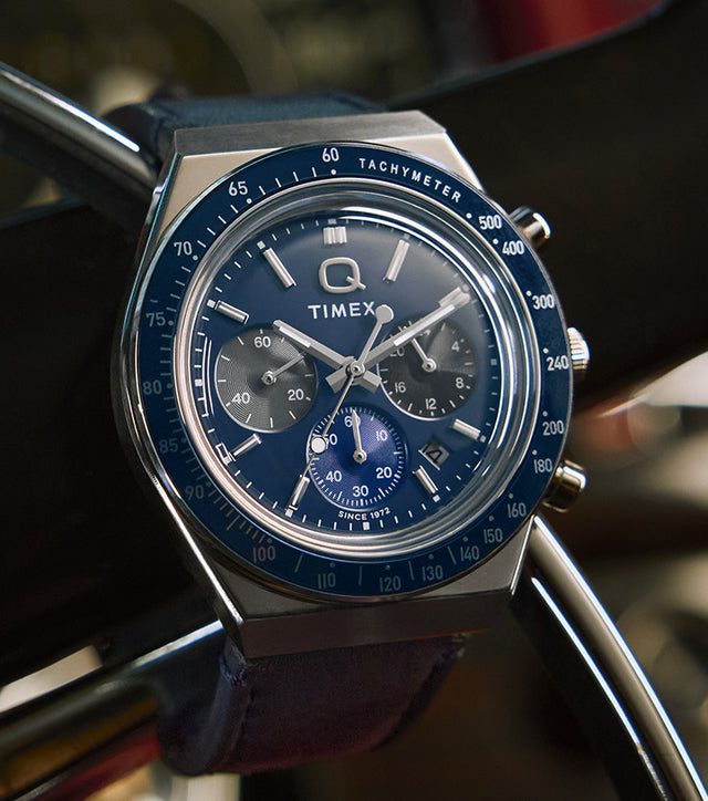Q Timex® Chronograph on a steering wheel—blue dial, three sub-dials, tachymeter bezel, date at 4 o’clock.