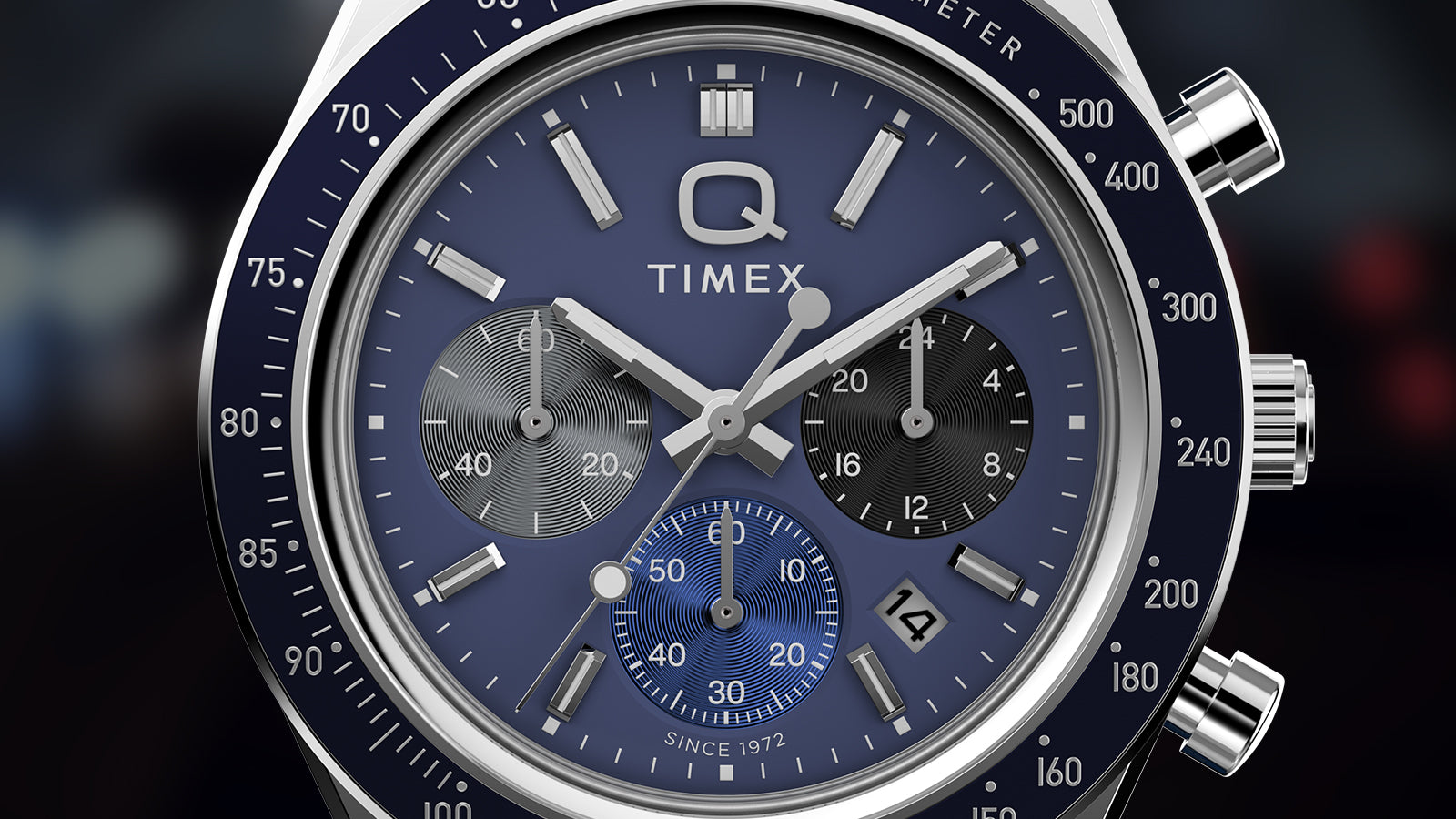 Close-up of the Q Timex® Chronograph dial showing blue face, three sub-dials, tachymeter scale, and date at 4 o’clock.