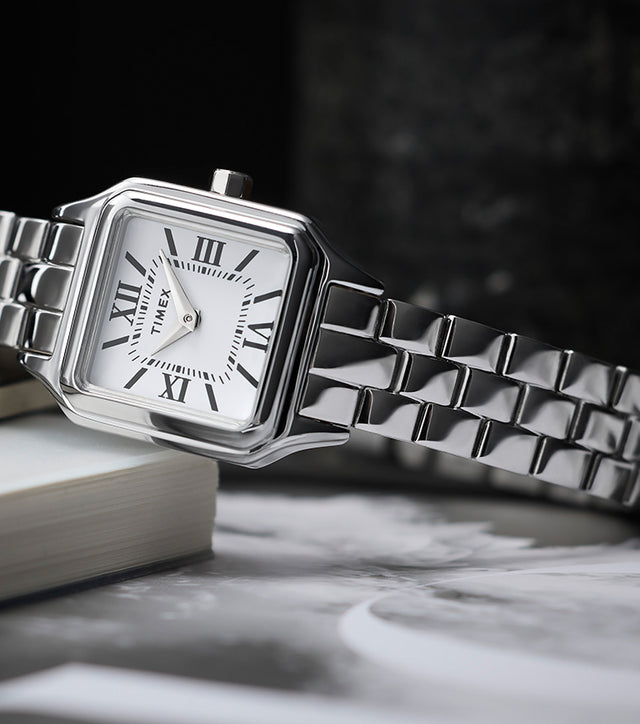 Timex Legacy Addison silver-tone women’s watch with square, rounded-corner case, white dial with black Roman numerals, and polished link bracelet, styled on books.