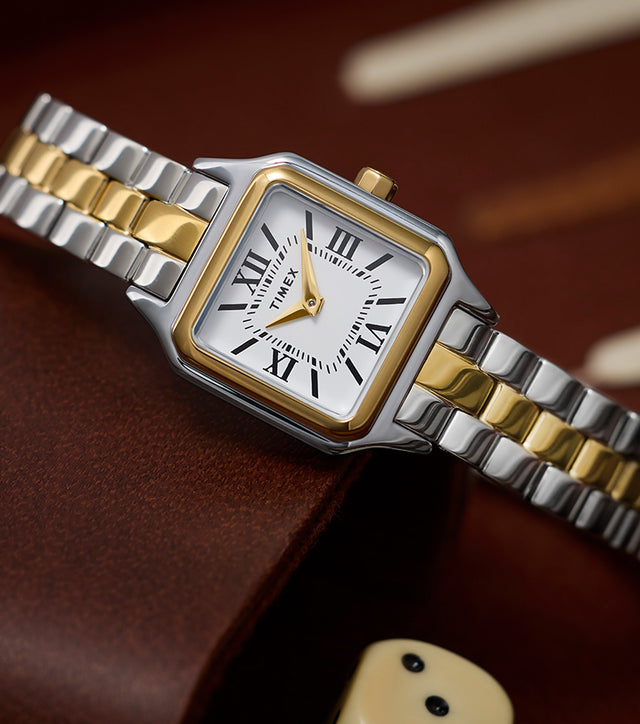 Timex Legacy Addison two-tone (silver and gold) women’s watch with square case and white Roman-numeral dial, styled on a backgammon board.