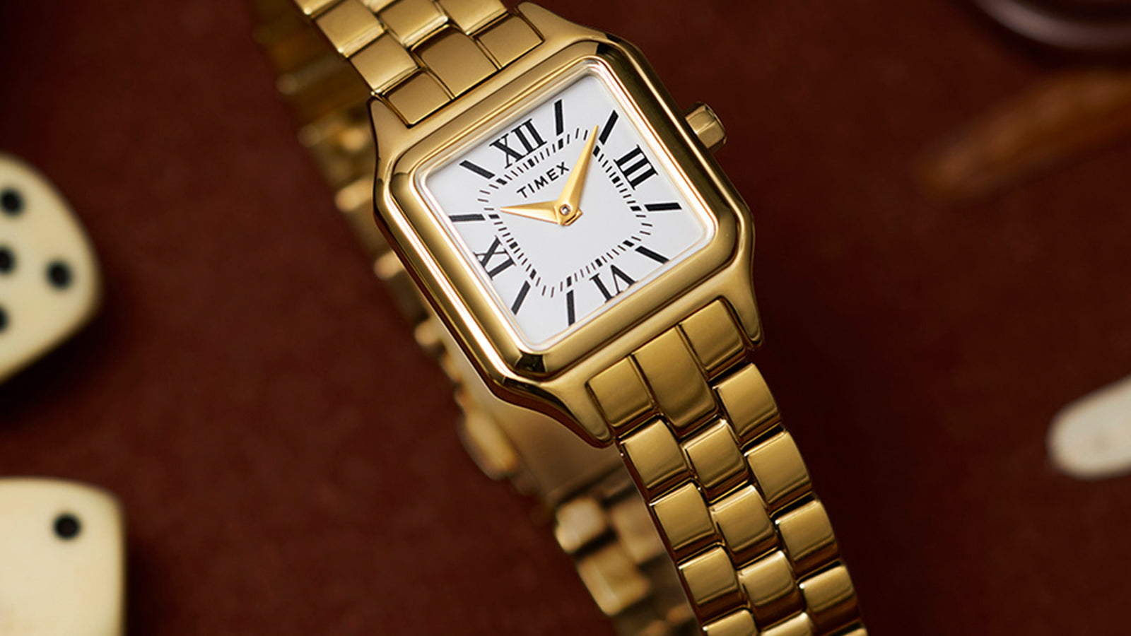 Timex Legacy Addison gold-tone women’s watch with rectangular case, white dial, and Roman numerals, styled on a backgammon board with dice.