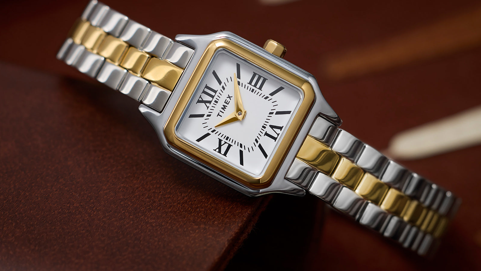 Timex Legacy Addison two-tone (silver and gold) women’s watch with square case and white Roman-numeral dial, styled on a backgammon board.