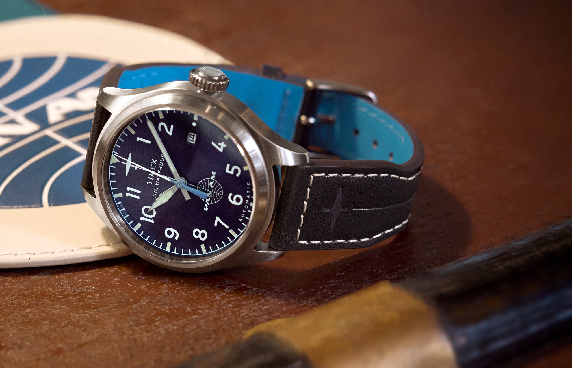 Close-up of the Timex x Pan Am® Waterbury Ace with a navy blue dial, bold white numerals, stainless steel case, and black leather strap featuring white stitching and embossed airplane detail.