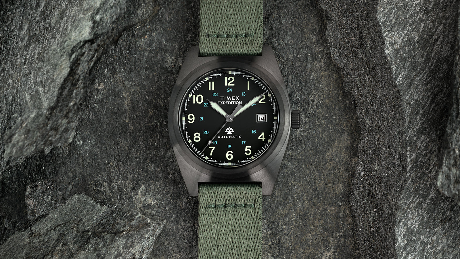 Front-facing view of the Timex Expedition® Capstone Automatic with a gunmetal case and green strap. The luminous dial and bold hour markers reflect a rugged, adventure-inspired aesthetic designed for outdoor performance.