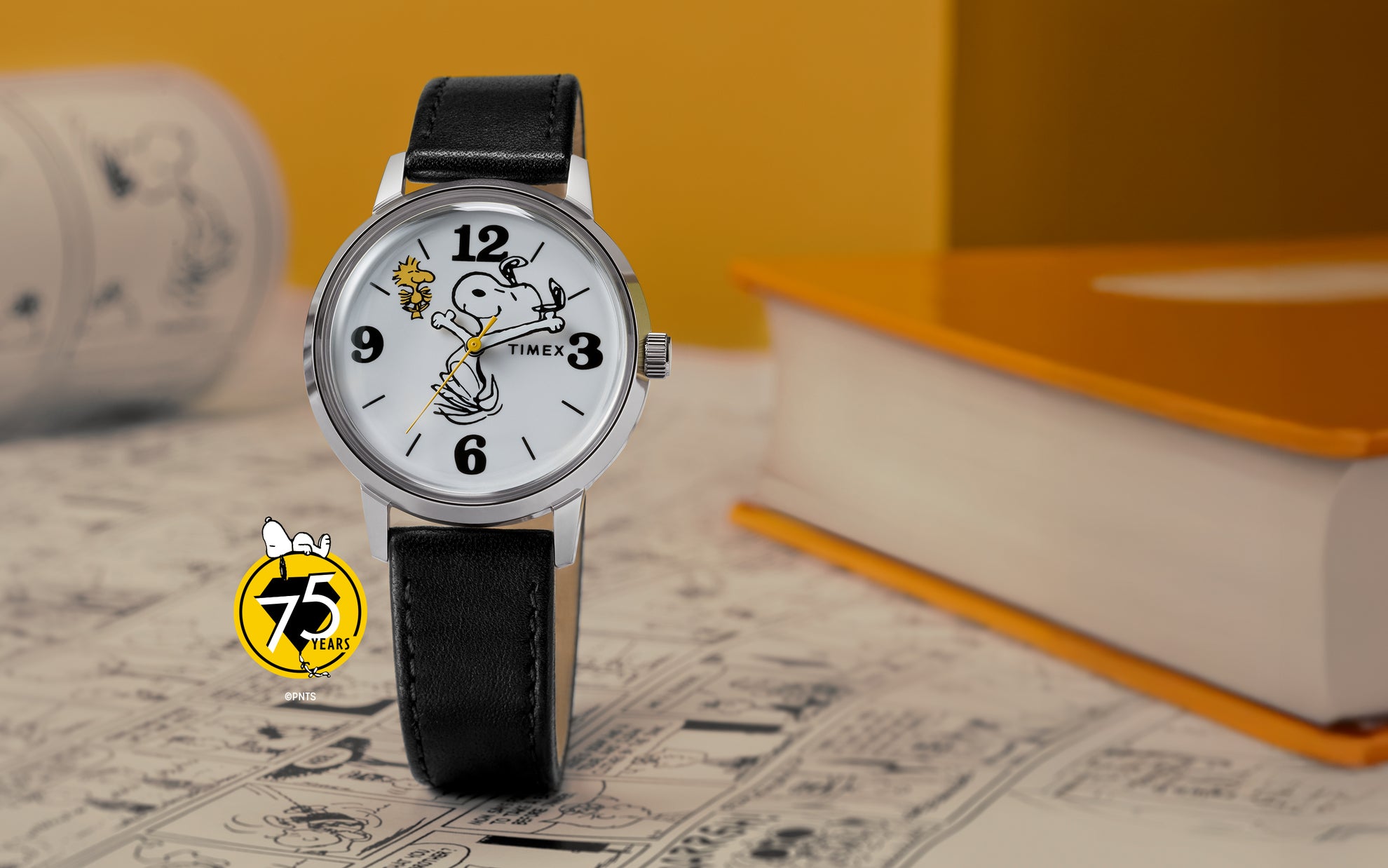 A Timex x Peanuts® Marlin® 75th Anniversary Edition watch with a white dial, black leather strap, and polished stainless-steel case displayed on a comic-themed background. The dial features Snoopy swinging a golf club with Woodstock flying nearby, and a yellow Peanuts 75 Years logo accent in the corner.