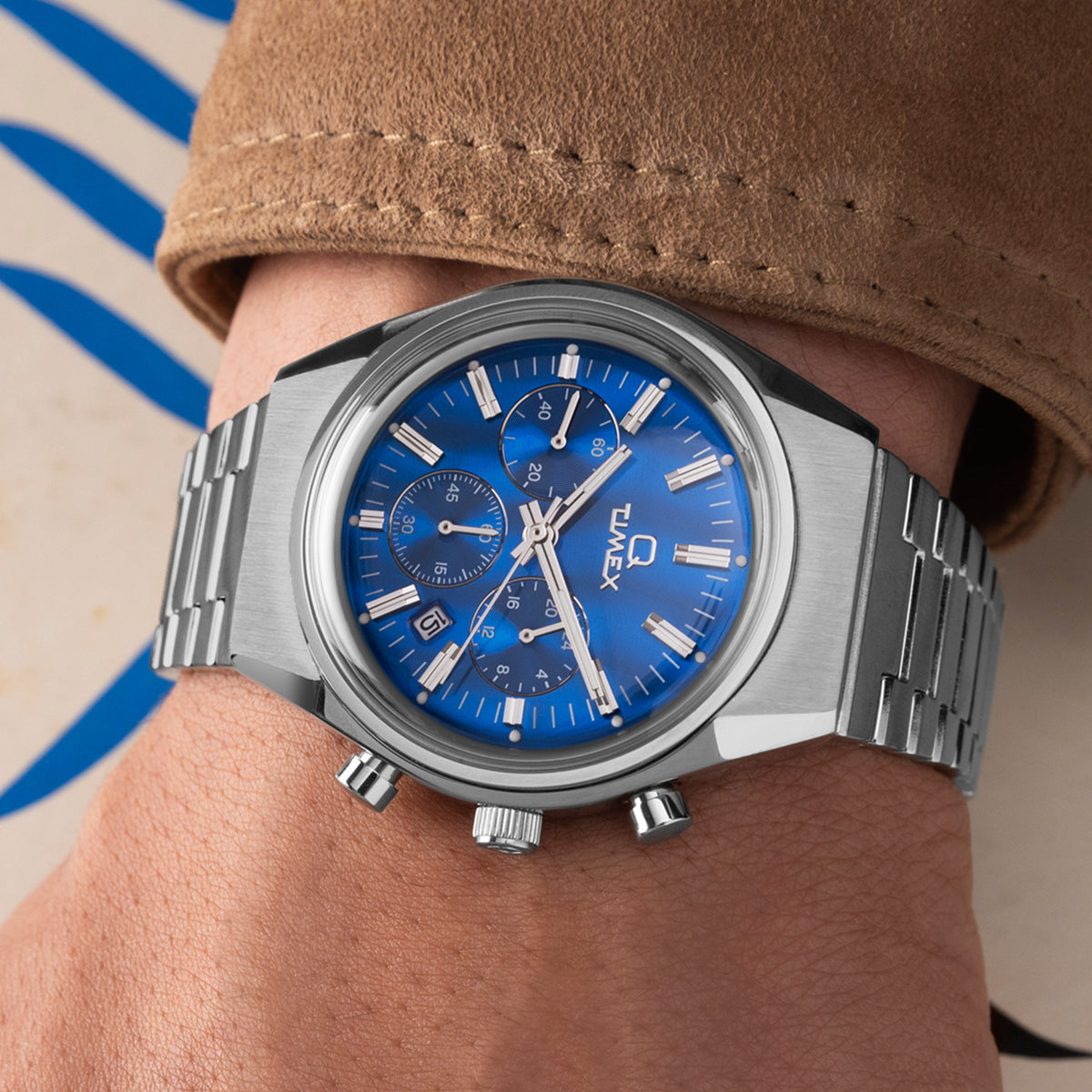 Side profile of the Q Timex Falcon Eye Chronograph emphasizing the domed crystal, brushed case edges, and solid stainless-steel bracelet links against a neutral gray background.
