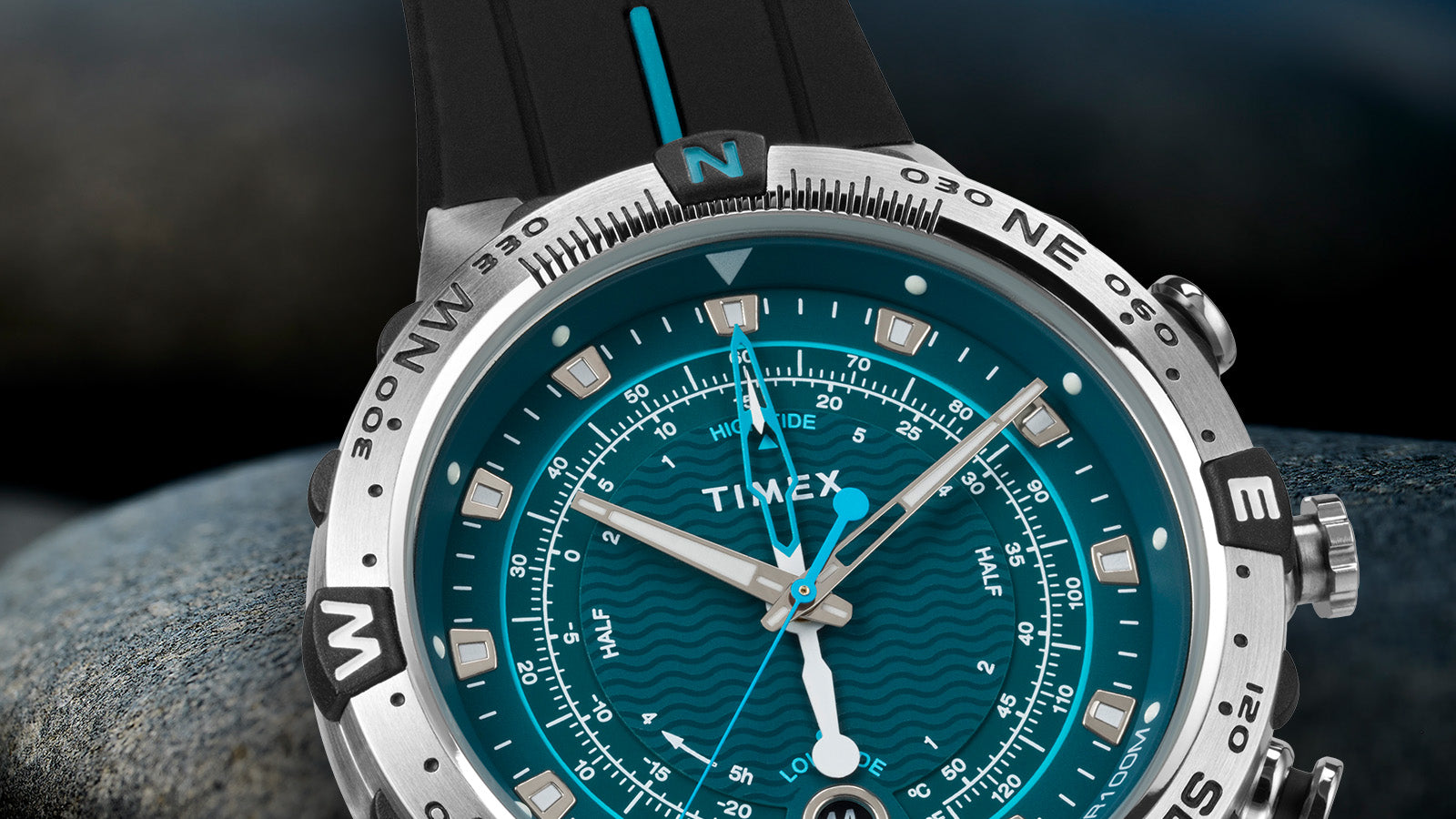 Macro shot of the Timex Expedition Tide-Temp-Compass bezel and dial, emphasizing the teal face with tide-tracking scale, compass bezel markers, and luminous white indices.