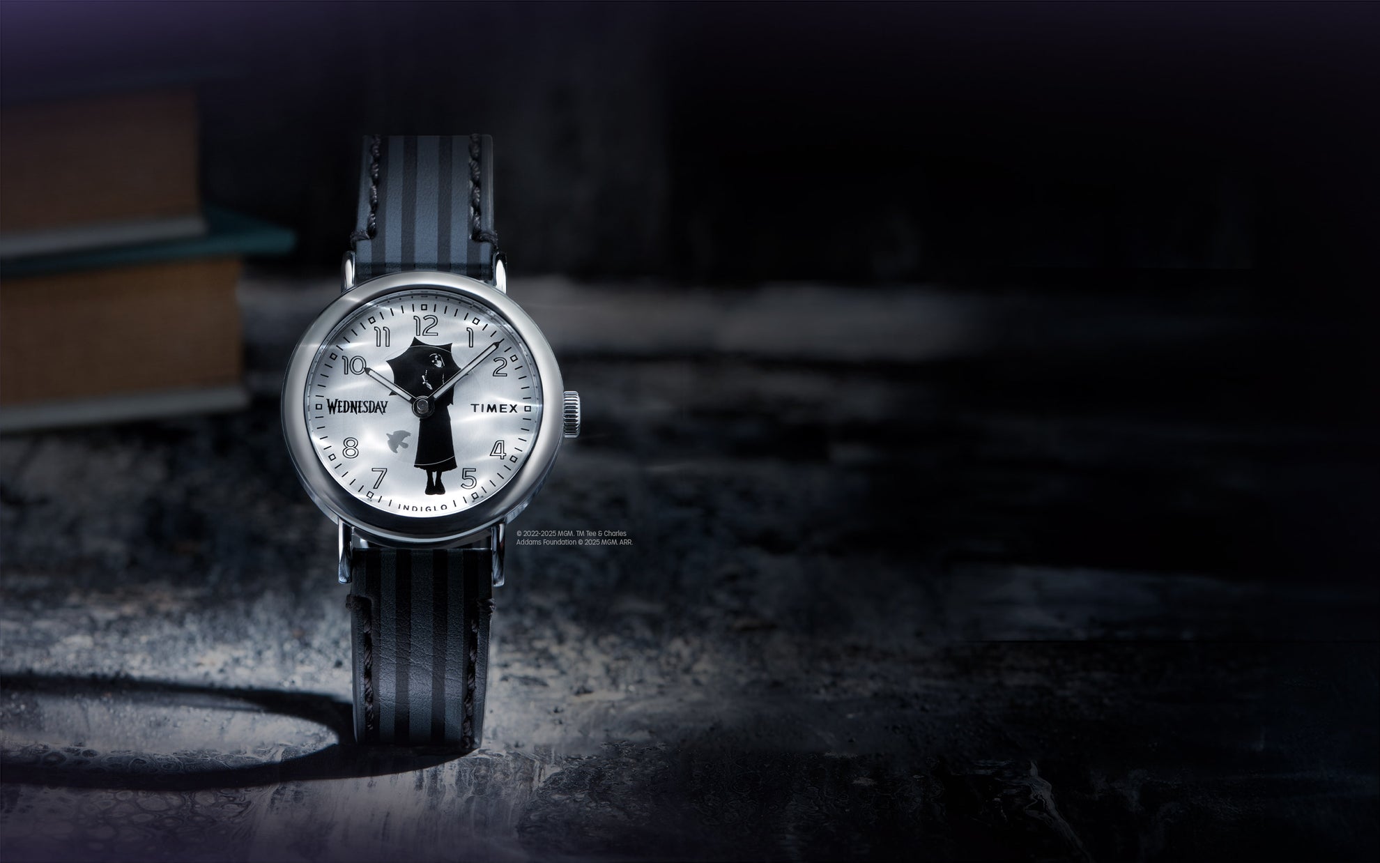 Flatlay of the Timex x Wednesday watch resting on a dark surface with a blurred book in the background, evoking a mysterious, academic aesthetic.