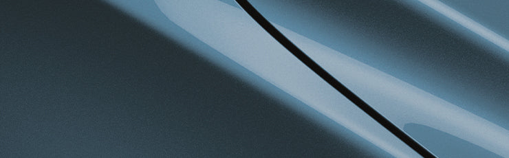 A close-up of glossy blue automotive paint with sharp diagonal reflections, suggesting speed and precision. The abstract background sets a sleek, modern tone.