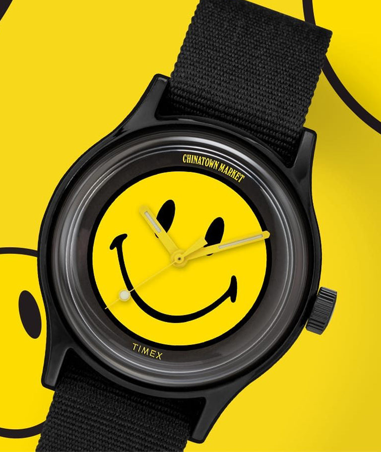 A watch with a smiley face on its dial and in the background