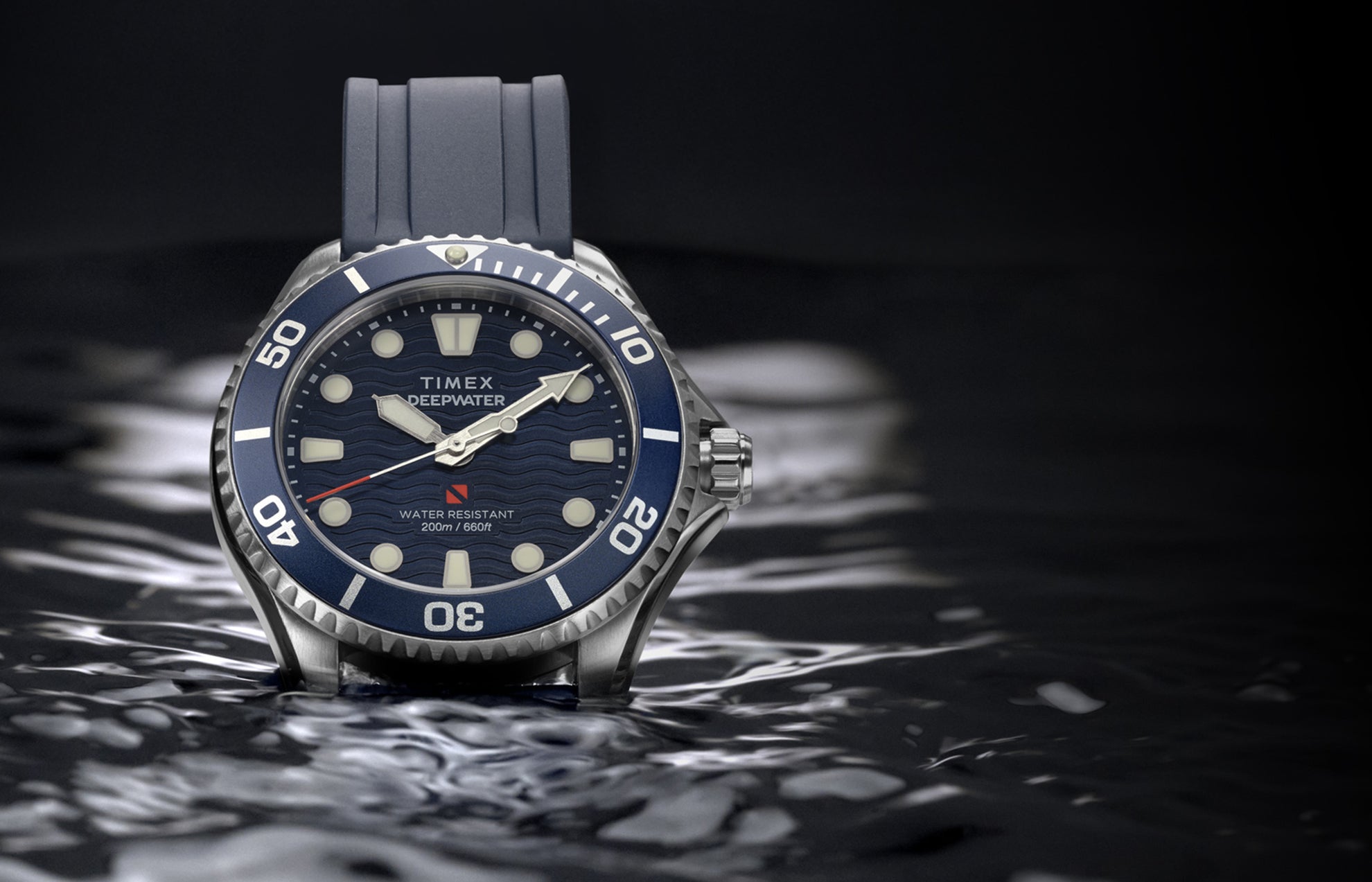 Timex Deepwater Meridian 200 with a blue strap and wave-pattern dial resting on the surface of dark water.