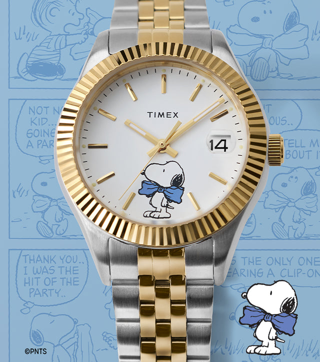 Timex x Peanuts® Timex Legacy watch in silver and gold-tone with white dial and Snoopy in a blue bow tie, displayed against a blue background with Peanuts® comic strip panels.