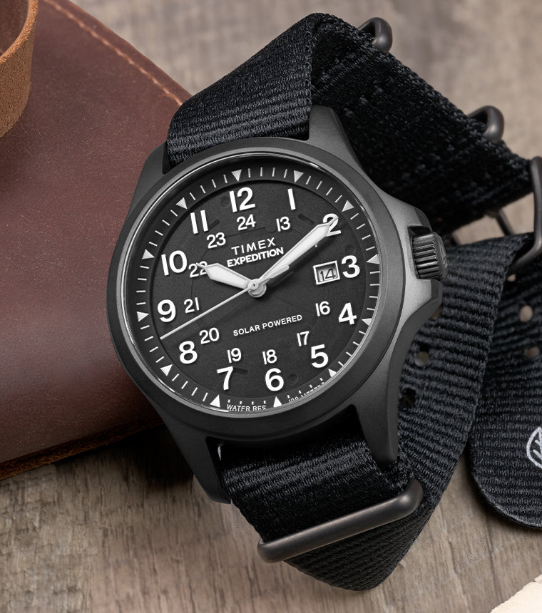 Expedition Field Post Solar watch with black dial and strap on wood surface – Timex Expedition® Field Post Solar watch with matte black case, black dial, and black fabric strap, placed beside a leather pouch and vintage map.