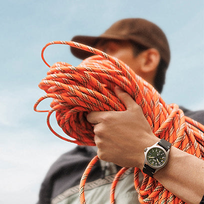 A man in outdoor gear holds a coil of orange climbing rope, wearing the Timex Expedition® Field Post Solar watch on his wrist.