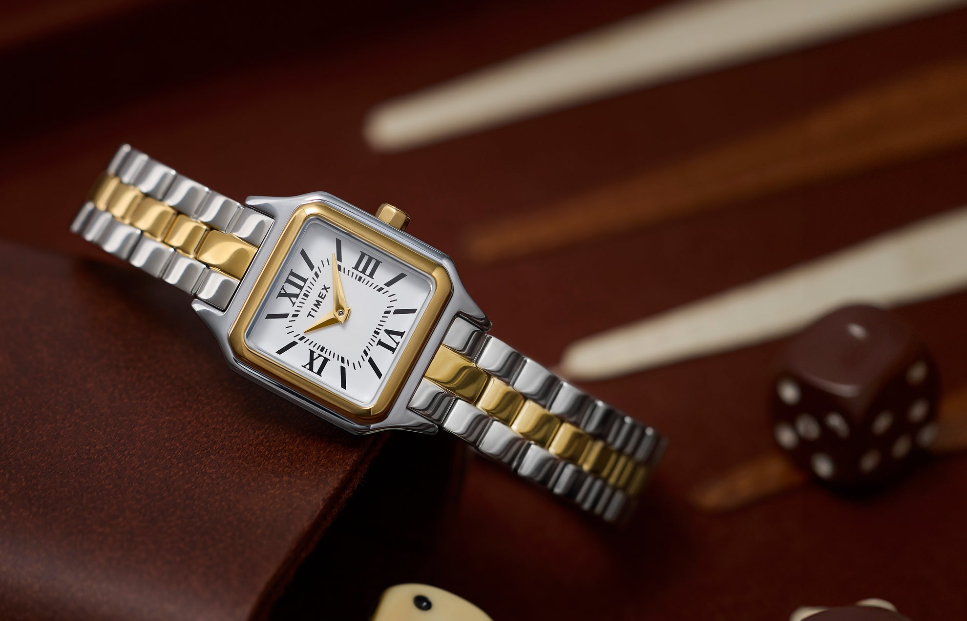 Timex Legacy Addison two-tone (silver and gold) women’s watch with square case and white Roman-numeral dial, styled on a backgammon board.