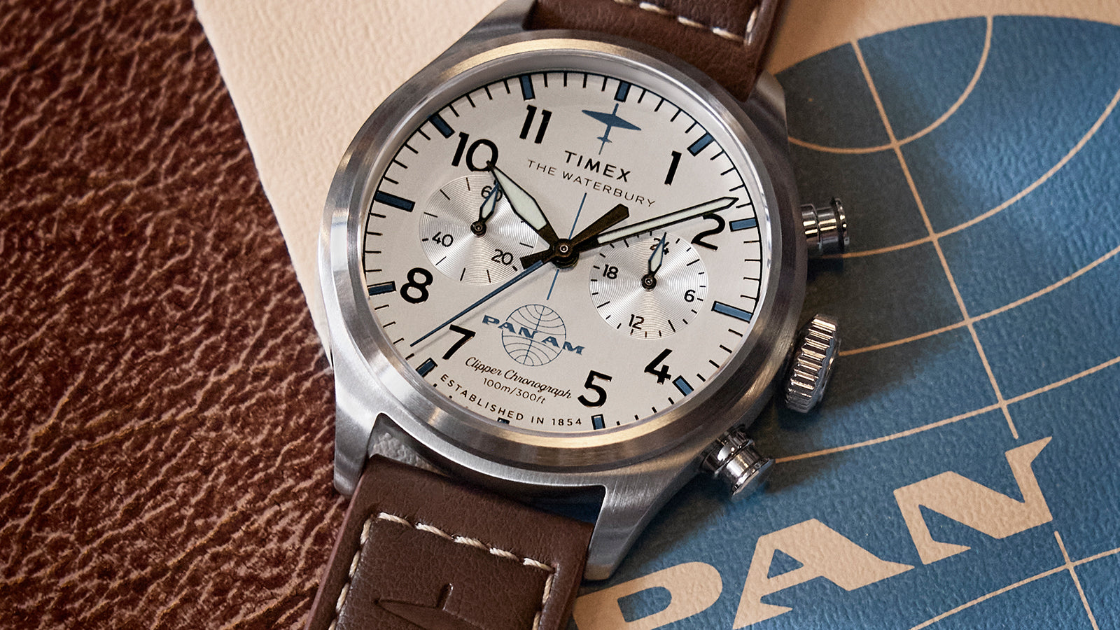 Close-up of the Timex x Pan Am® Waterbury Ace Chronograph with a white dial, black numerals, and brown leather strap resting on vintage Pan Am travel documents.