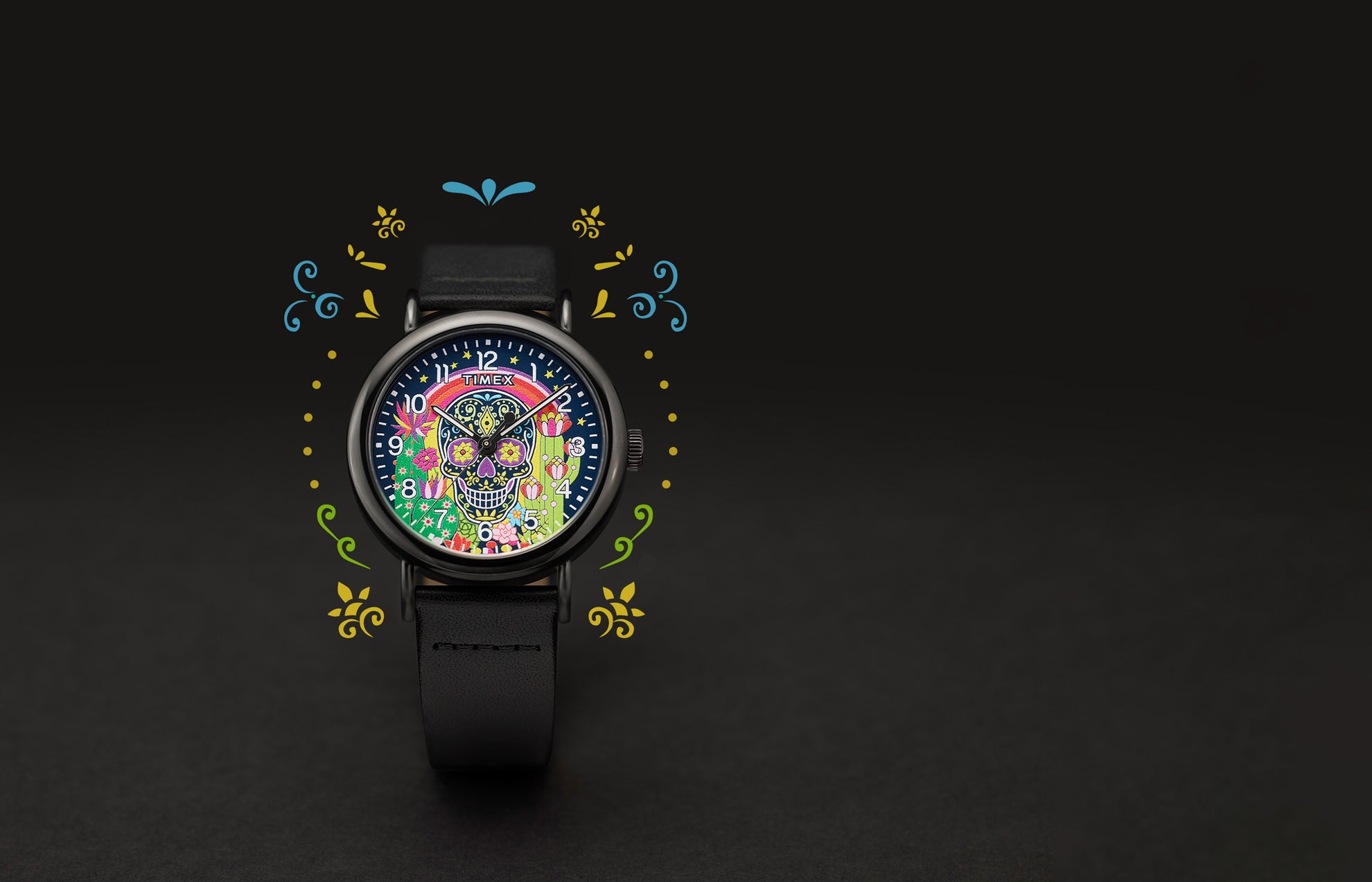 Timex Weekender Day of the Dead watch with a colorful sugar skull, rainbow, stars, and cactus floral design on the dial. The black leather strap is shown with decorative graphics surrounding the watch.