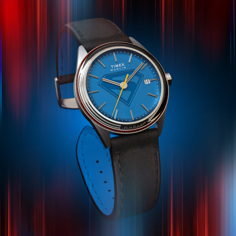 Timex x Superman Marlin watch featuring a bright blue dial with the Superman emblem, yellow seconds hand, silver-tone case, and black leather strap, set against a red and blue gradient background.