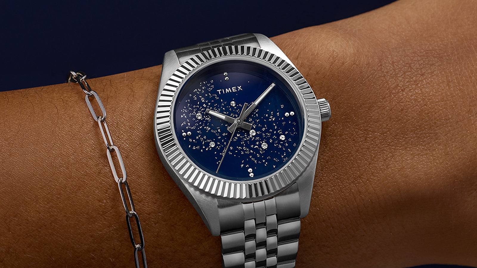 Timex Legacy watch worn on a wrist, featuring a blue starry dial and silver bracelet paired with a minimalist chain bracelet for an elegant look.