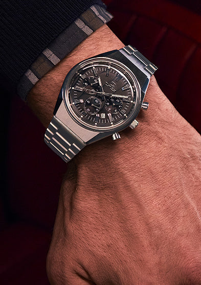 Person wearing the Q Timex Falcon Eye Chronograph while resting their arm in a vintage car interior with red leather seats, emphasizing the classic design.