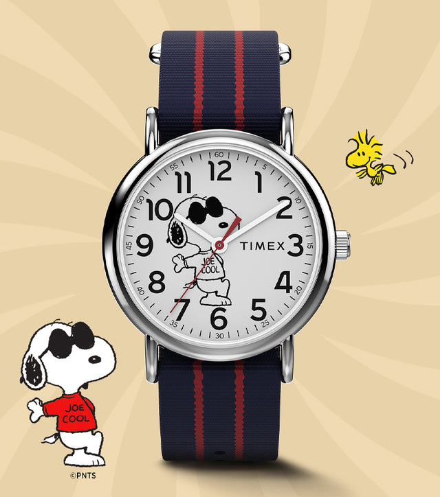Timex x Peanuts® Weekender watch featuring Snoopy as “Joe Cool” on the dial, paired with a navy and red-striped fabric strap. Displayed on a warm beige background with Snoopy and Woodstock illustrations for a playful, nostalgic look.