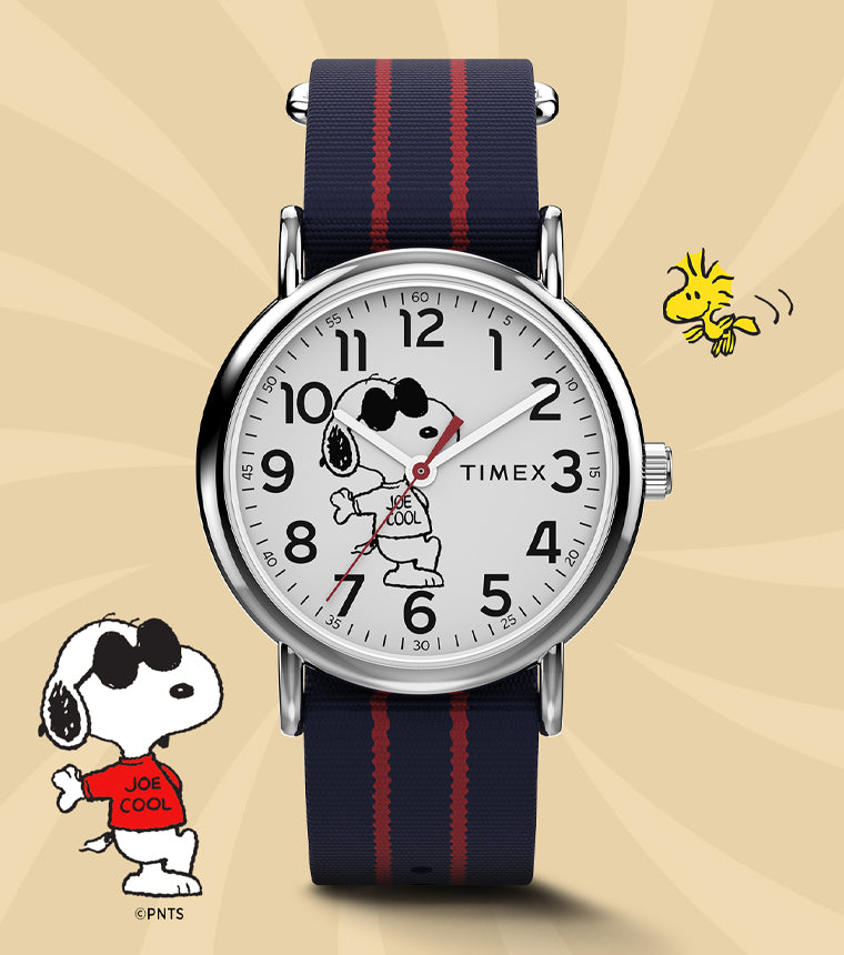 Timex x Peanuts® Weekender watch featuring Snoopy as “Joe Cool” on the dial, paired with a navy and red-striped fabric strap. Displayed on a warm beige background with Snoopy and Woodstock illustrations for a playful, nostalgic look.