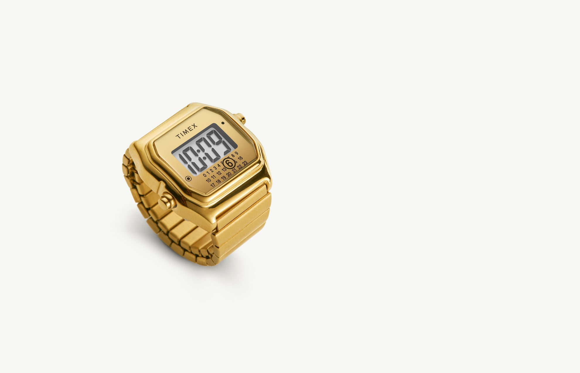 The Timex x MM6 Maison Margiela T80 digital watch in full gold-tone finish, featuring a square retro case, matching metal bracelet, and digital display. The minimalist dial includes the MM6 calendar-style date motif and Timex branding, set against a clean cream background.