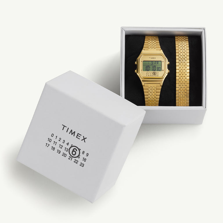 Timex x MM6 T80 watch displayed in its white gift box, which features the MM6 numeric logo design. The watch rests on black padding next to an extra gold-tone bracelet link.