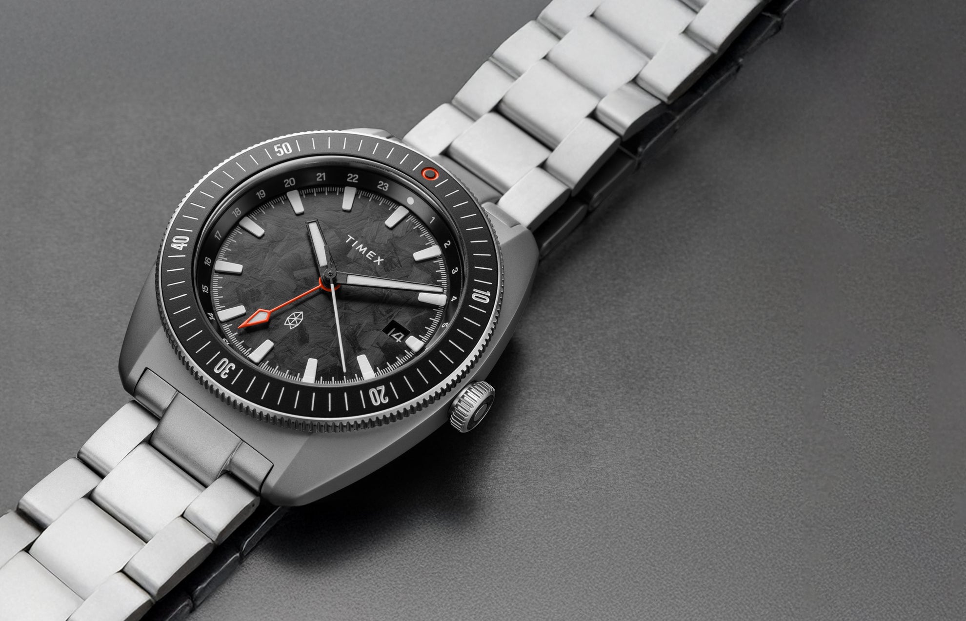 Close-up view of The James Brand x Timex GMT watch showing the black marbled dial, orange GMT hand, and stainless steel bracelet.