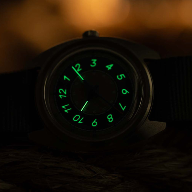 The Timex x Worn & Wound Storm watch in low light, with its numerals and hands glowing bright green against the darkened dial.