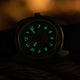 The Timex x Worn & Wound Storm watch in low light, with its numerals and hands glowing bright green against the darkened dial.