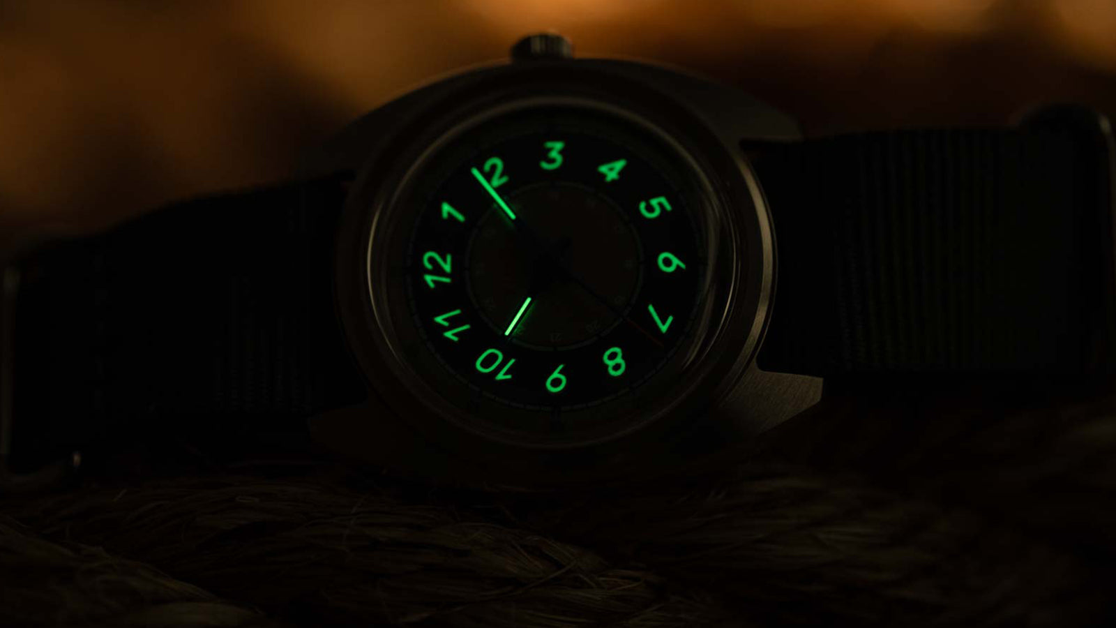 The Timex x Worn & Wound Storm watch in low light, with its numerals and hands glowing bright green against the darkened dial.