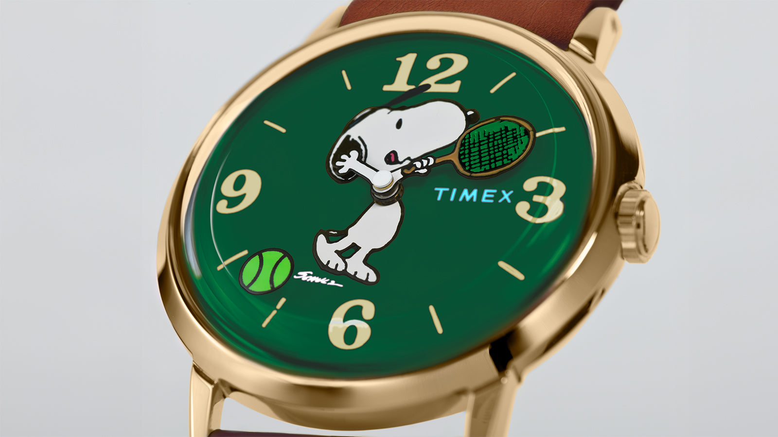 Close-up of the Timex Marlin® Hand-Wound x Snoopy Tennis watch dial showing Snoopy swinging a tennis racket on a green background with gold-tone numerals and a tennis ball near 6 o’clock.