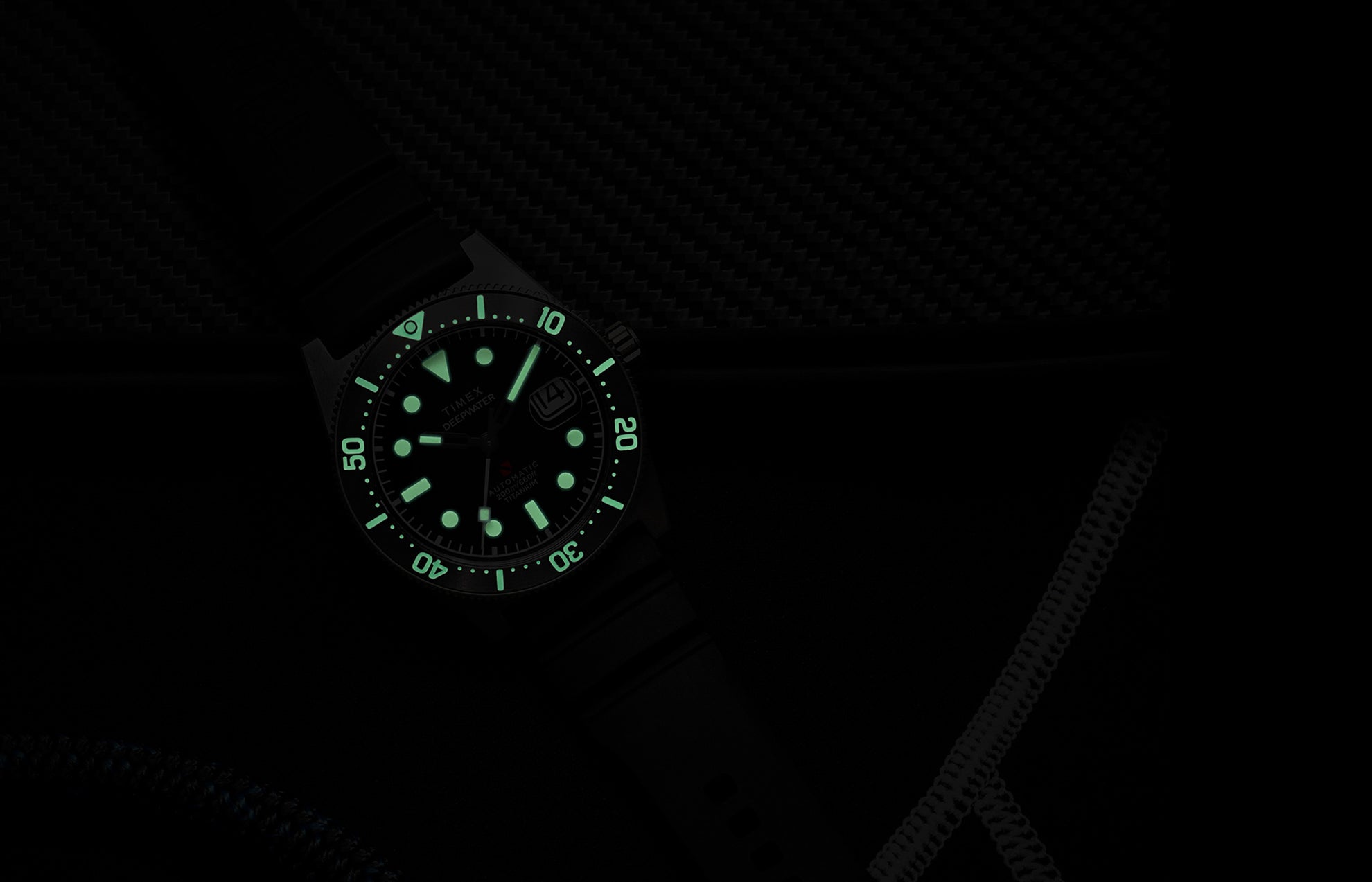 Timex Deepwater Reef 200 Titanium Automatic watch glowing in the dark, showing strong luminescence on the dial and bezel markers against a dark background.