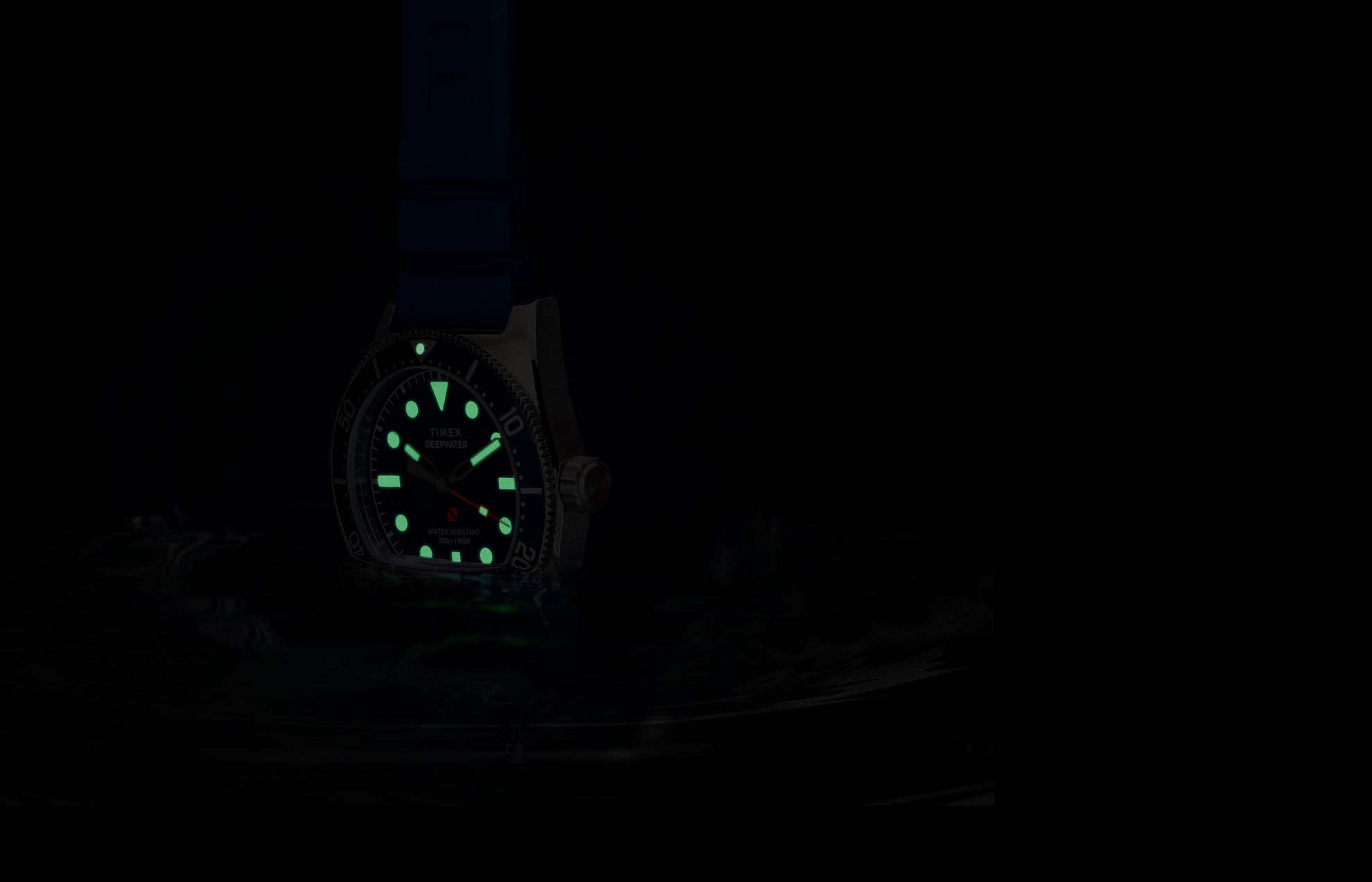 Timex Deepwater Reef 200 watch glowing underwater, with luminous markers and hands shining green in low light, emphasizing dive-ready legibility.