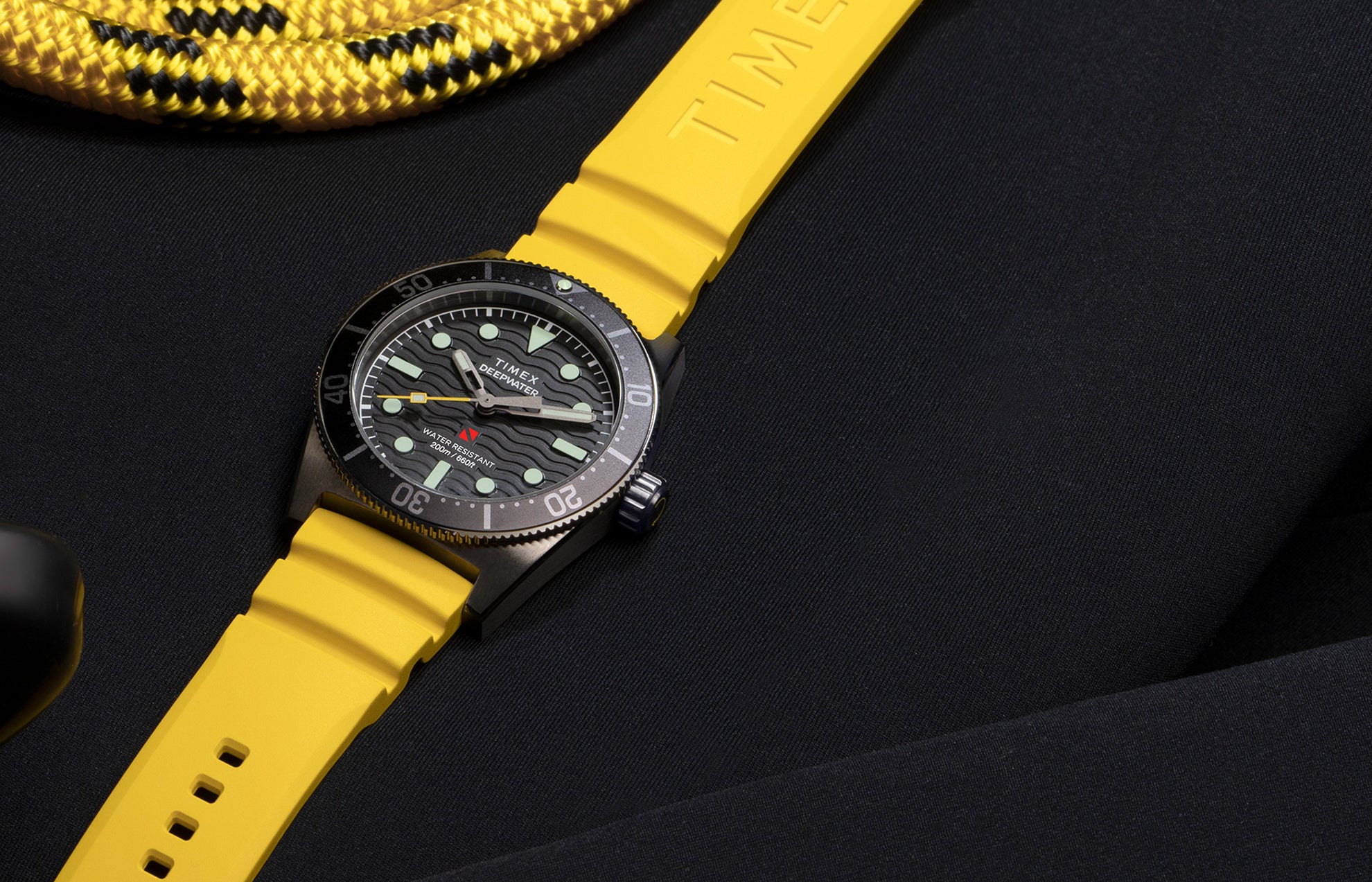 Timex Deepwater Reef 200 dive watch with black dial and bold yellow rubber strap, displayed on dark neoprene material with yellow diving rope, highlighting its rugged aquatic design.