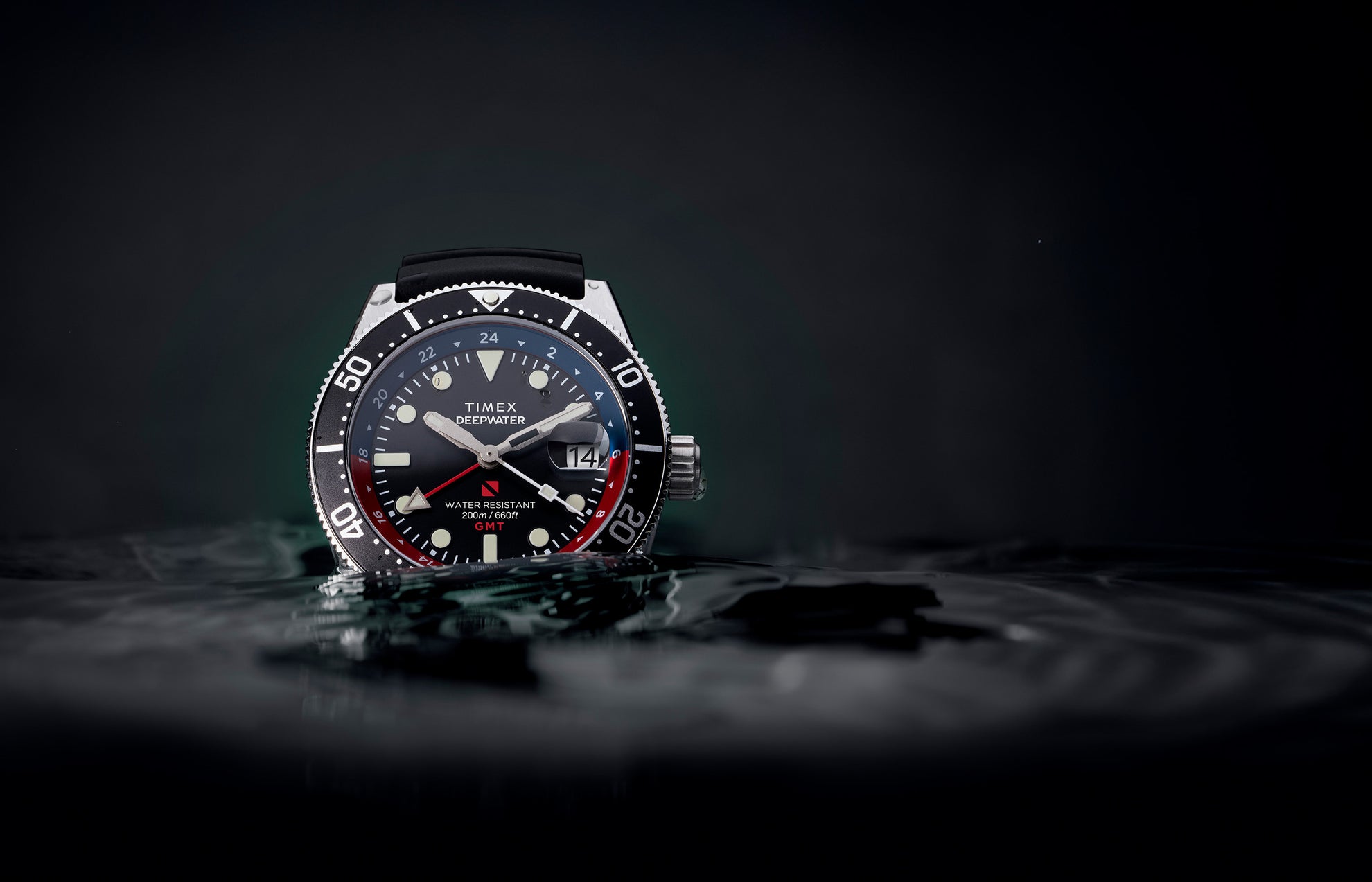 Timex Deepwater Reef 200 GMT dive watch with black dial, black strap, and red-blue bezel partially submerged in water, emphasizing its rugged design and 200-meter water resistance.