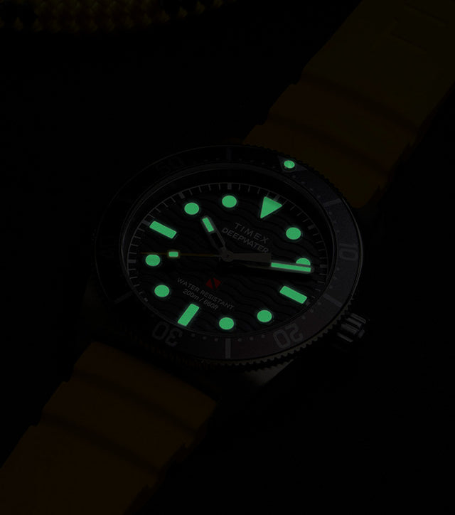 Timex Deepwater Reef 200 dive watch glowing in the dark, showing luminous hands and hour markers for enhanced underwater visibility.