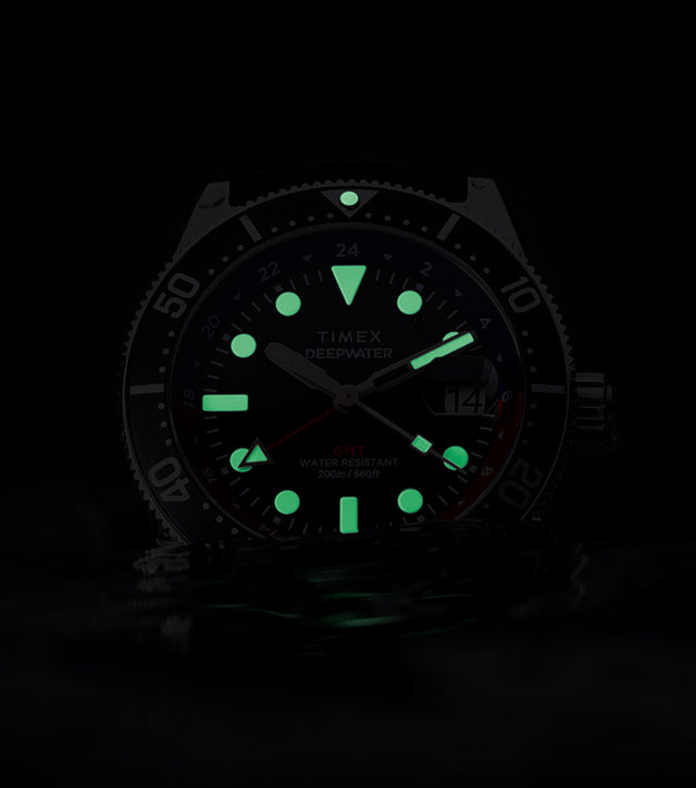 Timex Deepwater Reef 200 GMT glowing in darkness, showing bright green luminescent markers and hands for underwater visibility.