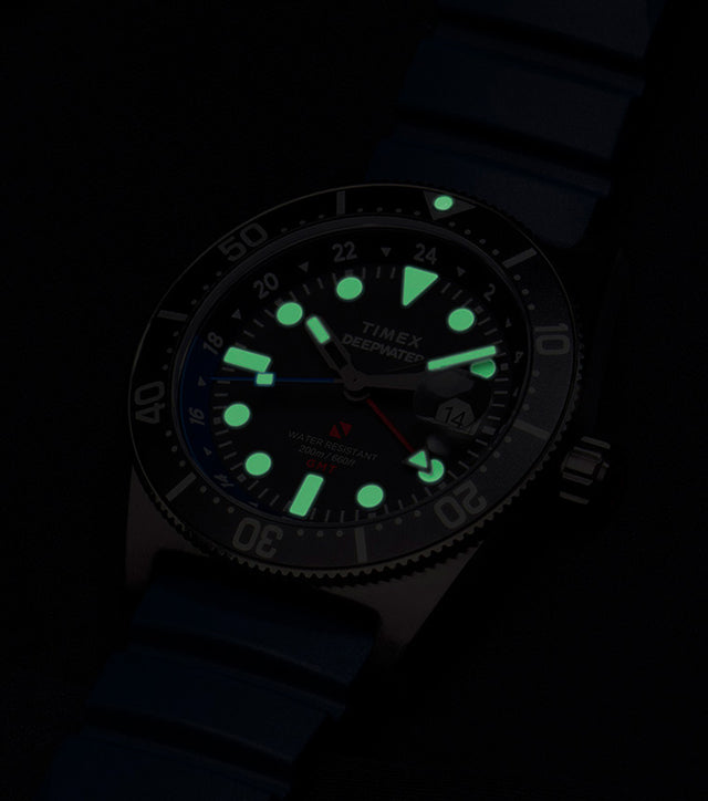 Timex Deepwater Reef 200 GMT glowing in the dark, showing bright green luminescent hour markers and hands for optimal underwater visibility.