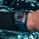 Diver wearing the Timex Deepwater Reef 200 watch underwater, the blue strap and stainless steel case reflecting light as bubbles rise around them.