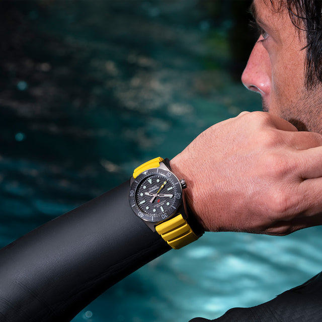 Diver wearing the Timex Deepwater Reef 200 with yellow strap, adjusting gear near the water’s surface, emphasizing sporty style and professional performance.