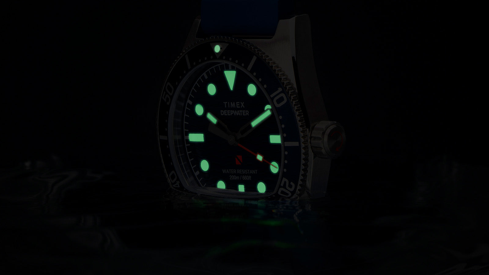 Timex Deepwater Reef 200 watch glowing underwater, with luminous markers and hands shining green in low light, emphasizing dive-ready legibility.