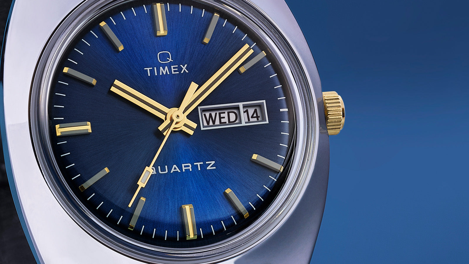 Close-up of the Q Timex® 1978 Day/Date dial highlighting the deep blue sunray finish, gold-tone hands and indices, and the day/date display at 3 o’clock.