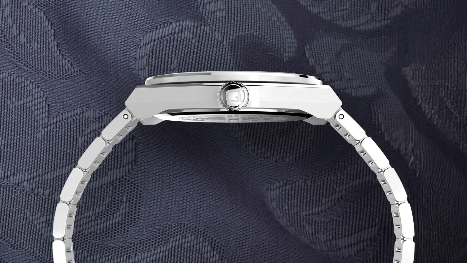 Profile view of the Q Timex® Continental GMT showing the brushed stainless-steel case, polished bezel edge, and the engraved “Q” logo crown.