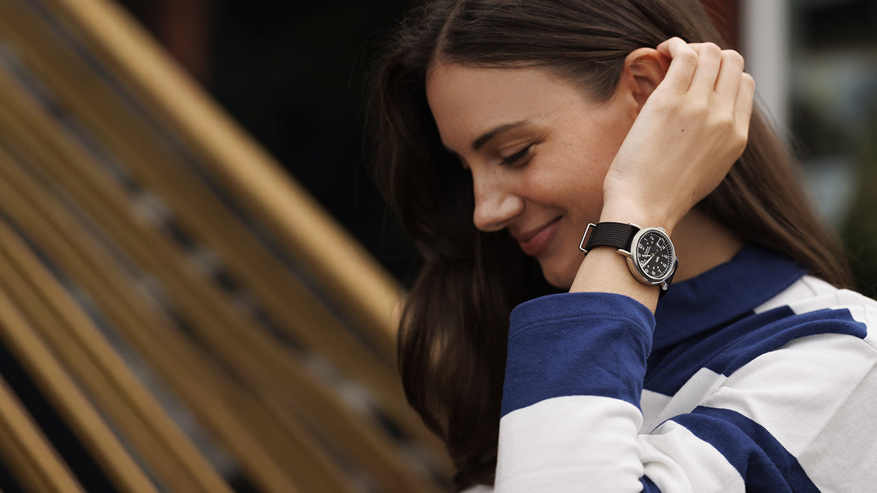 A woman smiling while wearing a Timex Weekender with a black dial and black fabric strap, paired with a navy and white striped top.