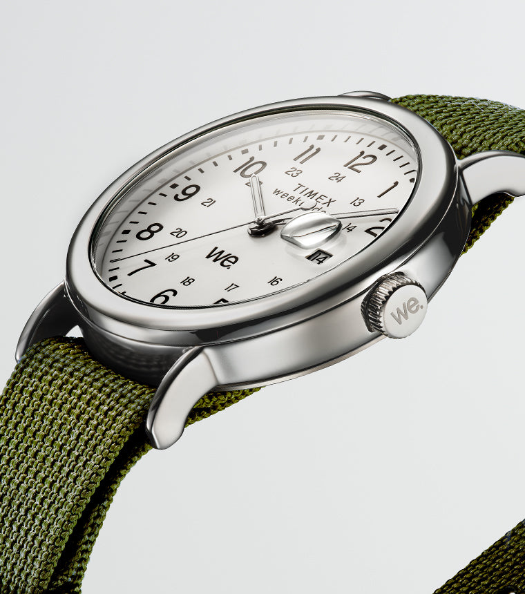 Angled view of a Timex Weekender watch with a green fabric strap, silver-tone case, and white dial with black numerals.