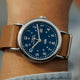 Close-up of the Timex Weekender watch with blue dial and brown leather strap worn on a wrist, paired with a denim shirt.
