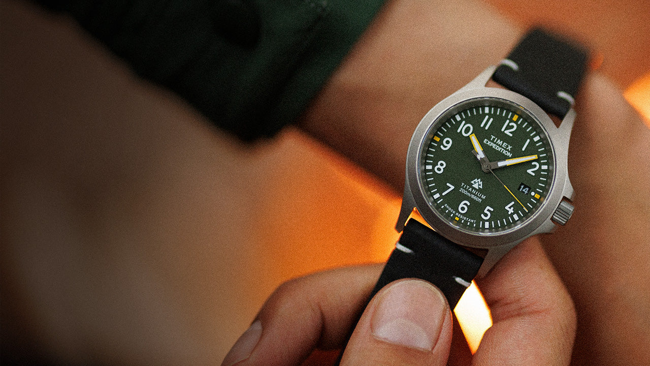 A Timex Expedition Titanium watch with a green dial, luminous white numerals, and black leather strap, worn on the wrist in warm lighting.